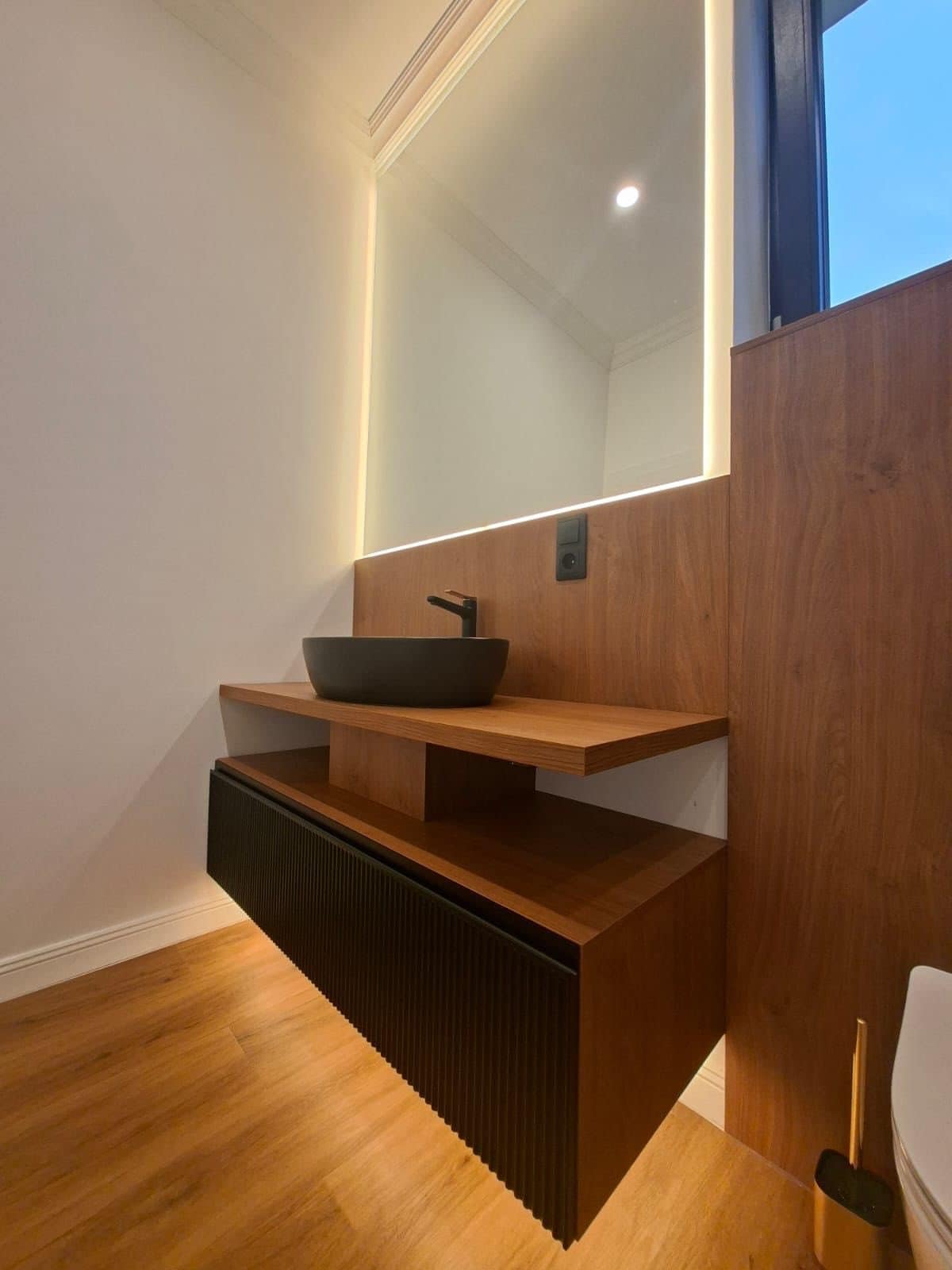 Mobilier de baie suspendat sub o oglindă cu lumină, lângă fereastră